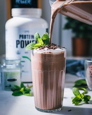Протеиновый коктейль с шоколадным вкусом в высоком стакане, украшенный свежей мятой и шоколадной стружкой, на фоне банки с протеиновым порошком — визуальное представление стратегии питания в период сушки, направленной на сохранение мышечной массы и достижение рельефа.